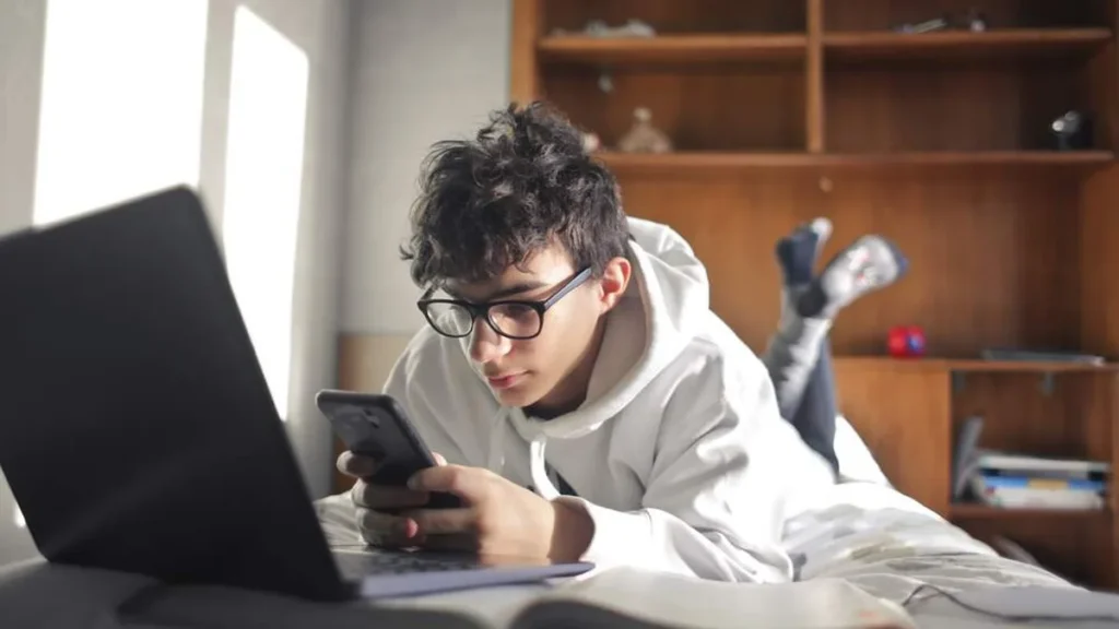 Imagem jovem usando celular junto com o notebook aberto do artigo Enem: Aplicativos digitais ajudam a organizar estudos