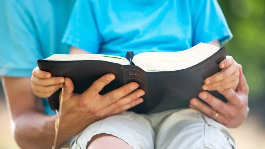 Imagem crianca lendo a biblia no colo do pai dela do artigo A palavra de Deus para as crianças