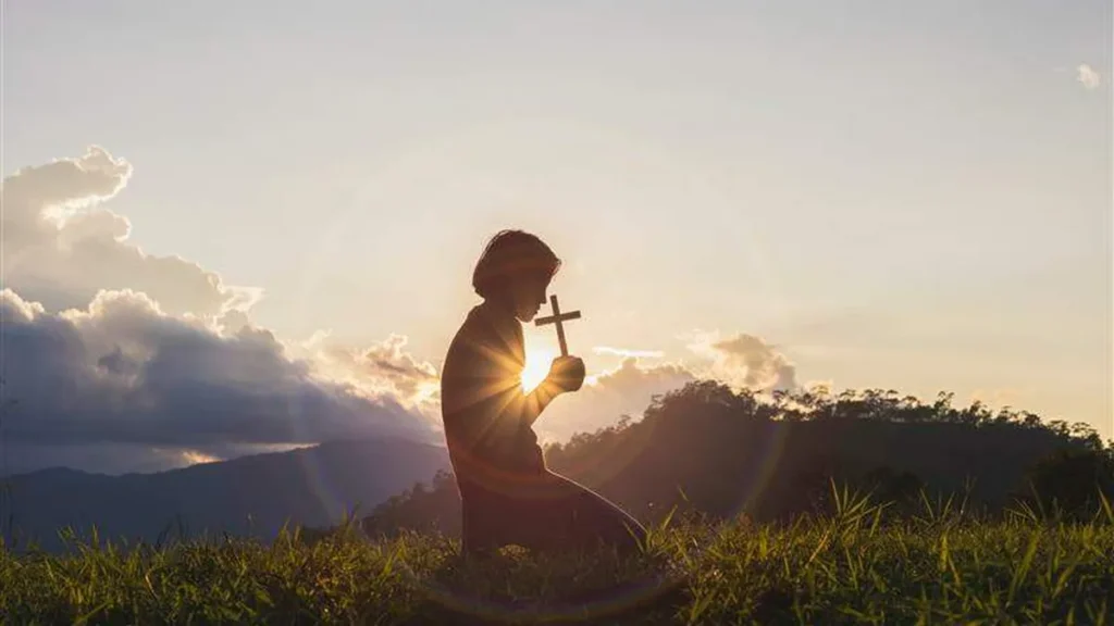 Imagem homem rezando de joelhos e segurando uma cruz na natureza do artigo O que Viktor Frankl revela sobre Deus e a cura?