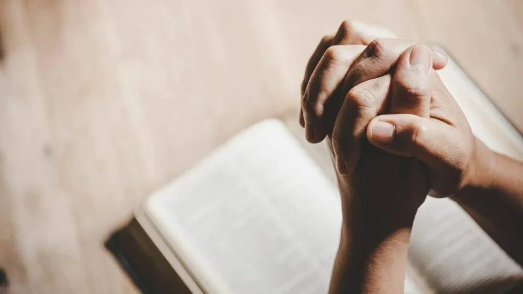 Imagem maos em oracao sob a Biblia do artigo 4 passagens da Bíblia para acalmar sua alma