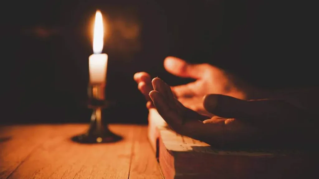 Imagem Maos voltadas para cima em oracao ao pai nosso com uma vela acesa ao fundo do artigo Confira 5 reflexões do Papa Francisco para viver o Natal