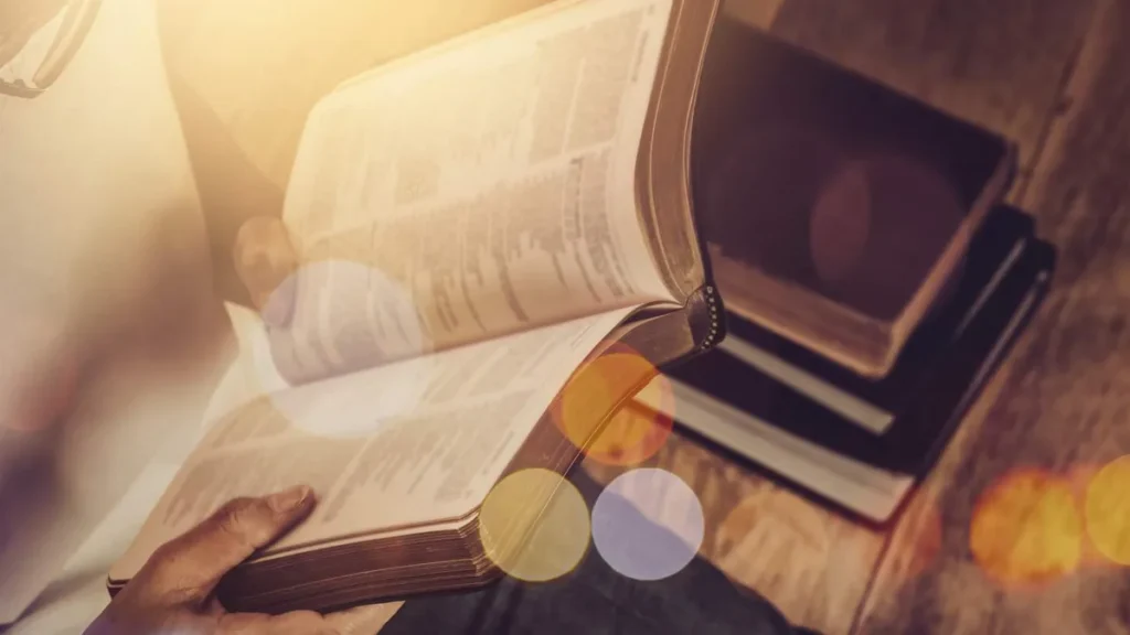 Imagem Biblia aberta nas maos de uma pessoa pagina turva na mesa de madeira com luz de janela do artigo Como a Bíblia pode me ajudar com a ansiedade e depressão?
