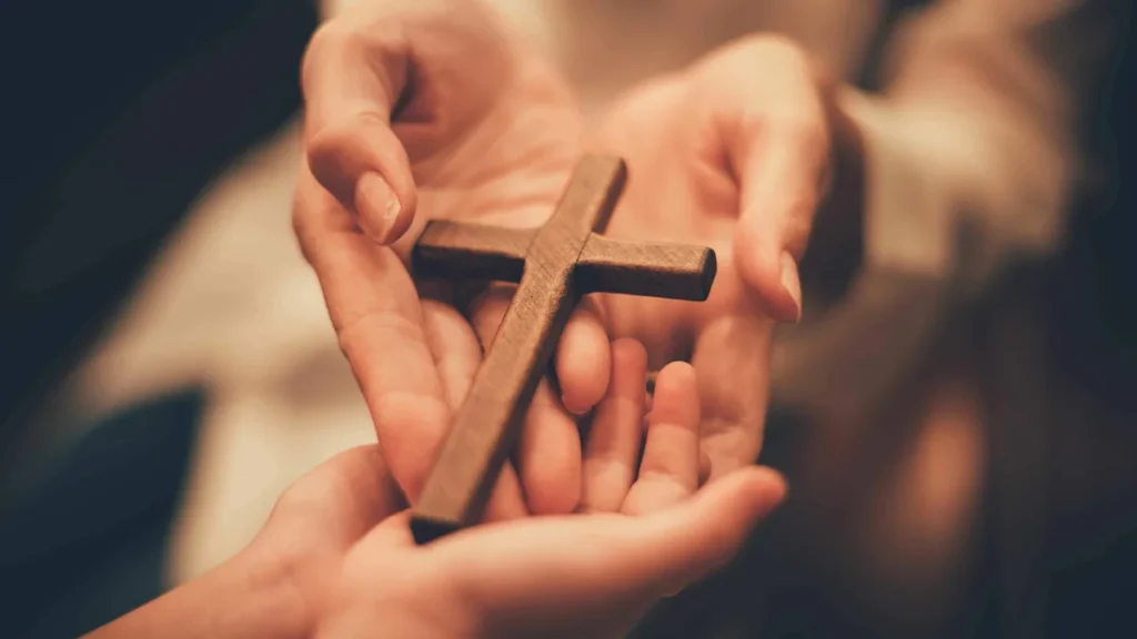 Imagem maos segurando uma cruz do artigo O amor de Deus age a todo momento