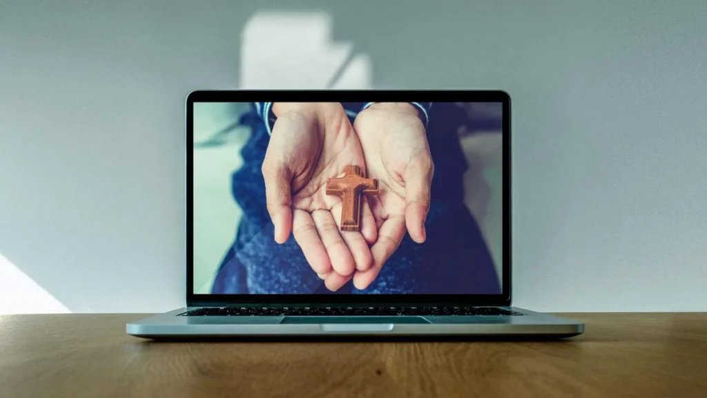 Imagem Maos segurando crucifixo na tela de um computador do artigo Confira a programação da Semana da Comunicação