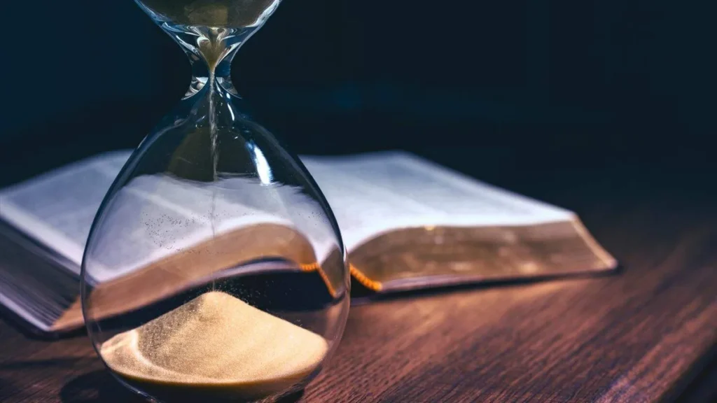 Imagem Biblia ao fundo desfocada com uma ampulheta na frente do artigo Como a Bíblia me ensina a ter paciência?
