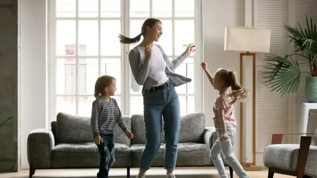 Mãe e filhos dançando na sala de casa.