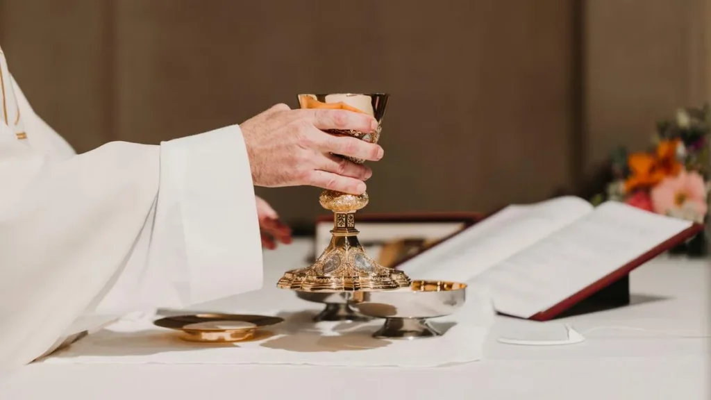 Imagem Padre segura calice do artigo Por que o sacerdote coloca mais vinho e pouca água no cálice?