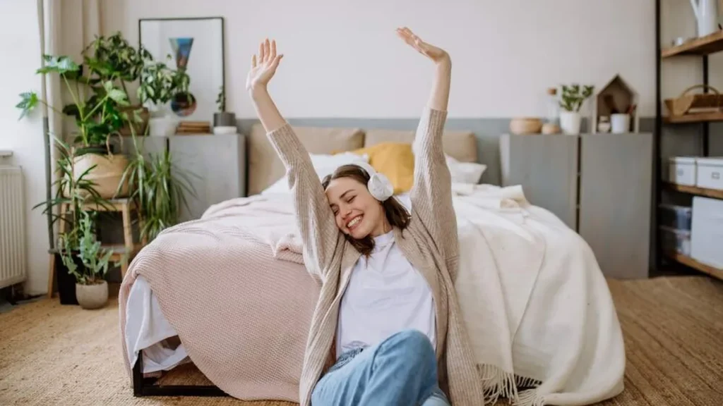 Moça em seu quarto ouvindo música com os braços pra cima