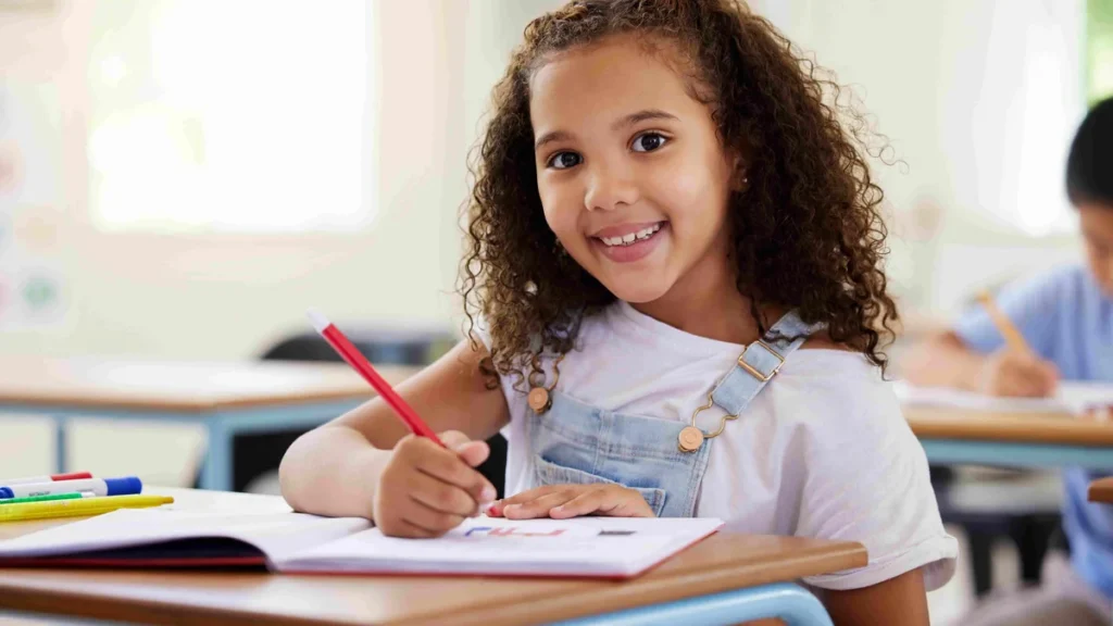 Imagem menina sentada em carteira escolar escrevendo do artigo Catequistas e pais: principais introdutores à vida cristã