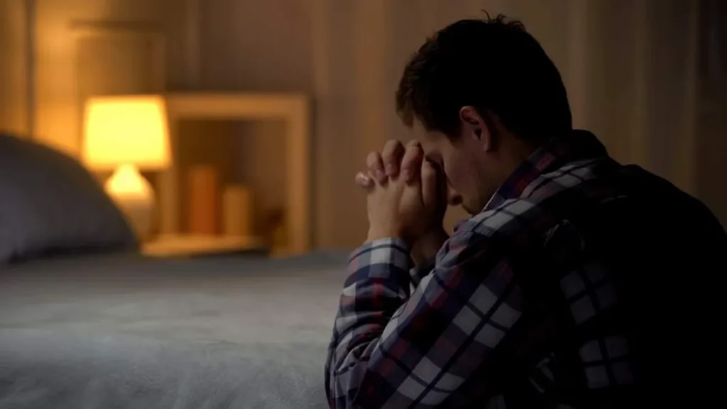 Imagem homem rezando em frente a cama do artigo Oração para encerrar seu dia com Deus