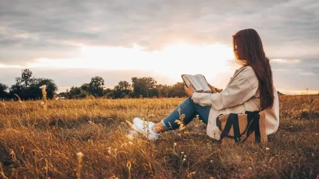 Imagem mulher jovem sentada na grama lendo a biblia do artigo A Bíblia nossa de cada dia