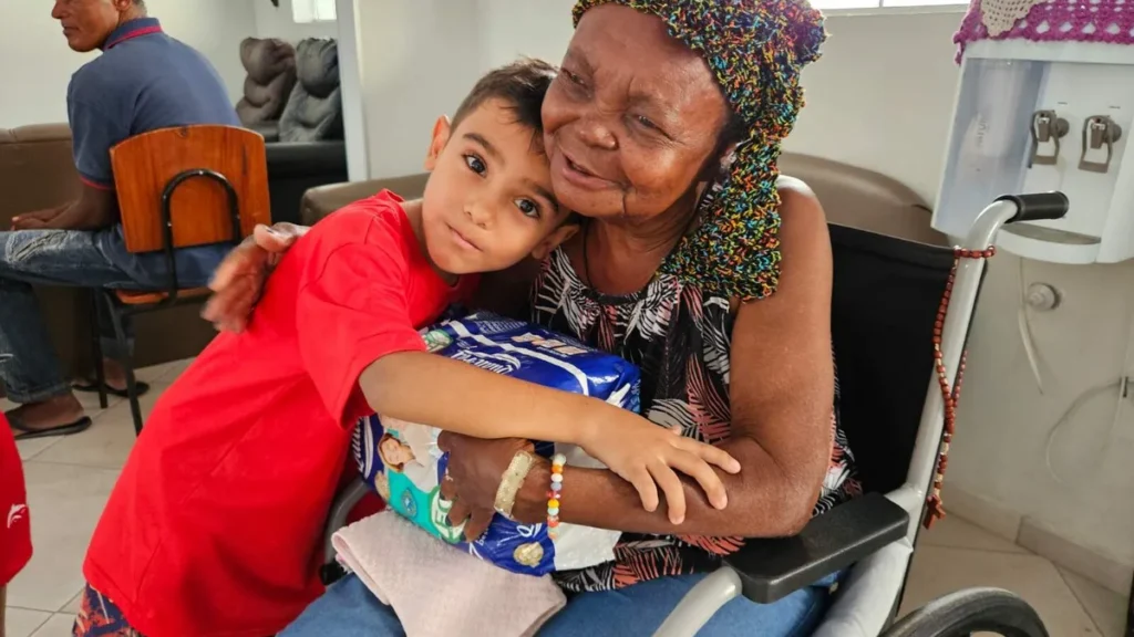 Criança entregando doação à idosa do Lar São Vicente, em Aparecida/SP