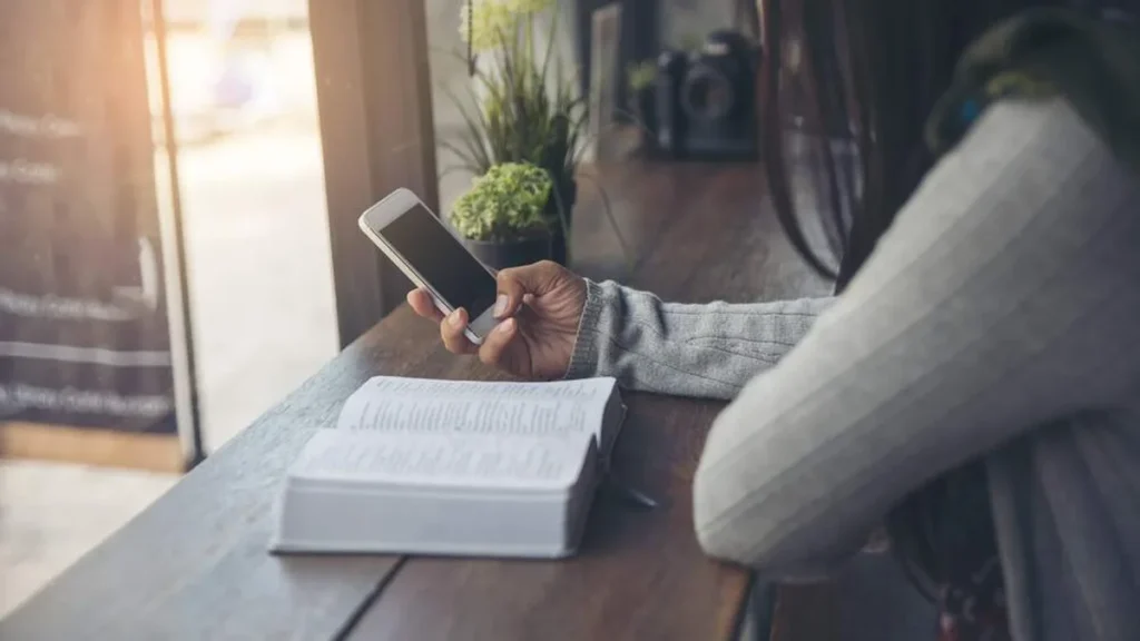 Imagem mulher mexe no celular e na biblia do artigo Evangelizar como um desafio constante no ambiente digital