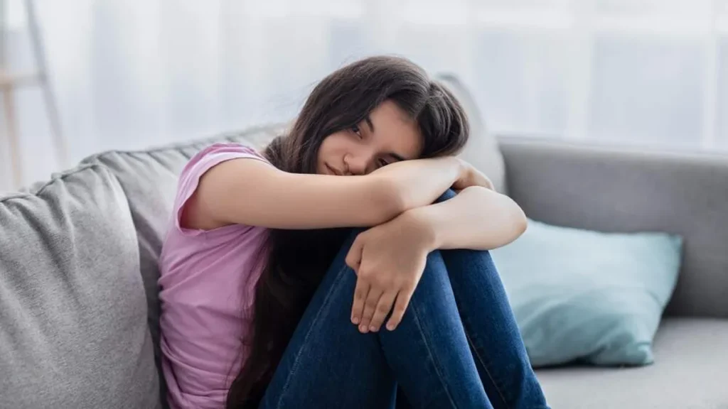 Imagem adolescente triste se abracando sentada no sofa do artigo Estou triste, o que posso fazer? 6 dicas para se sentir melhor!