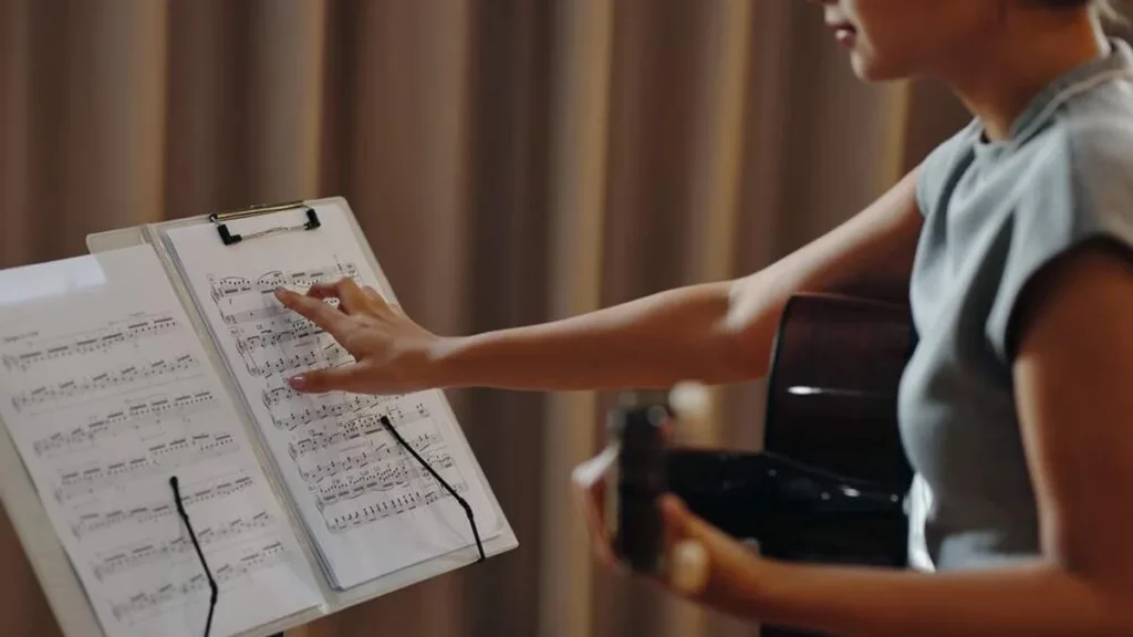 Imagem menina tocando violao com partitura do artigo PEMSA abre inscrições para oficinas de música em 2025