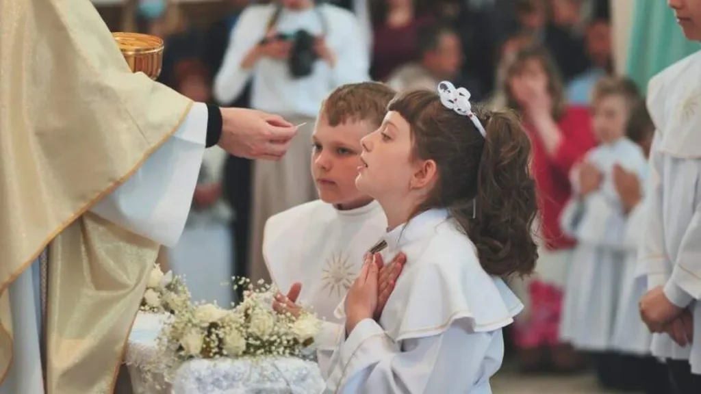 Imagem menina recebendo a comunhao do artigo O que as crianças precisam saber sobre rezar na Primeira Comunhão?
