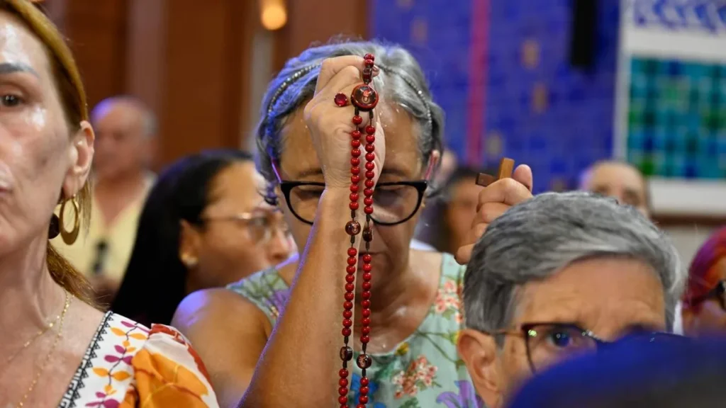 Imagem senhora ergue o terco na frente do rosto de olhos fechados rezando do artigo A ciência explica por que nos faz tão bem rezar o terço!