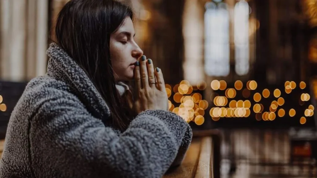 Imagem mulher rezando de joelhos na igreja do artigo Maria nos ensina a ser resilientes