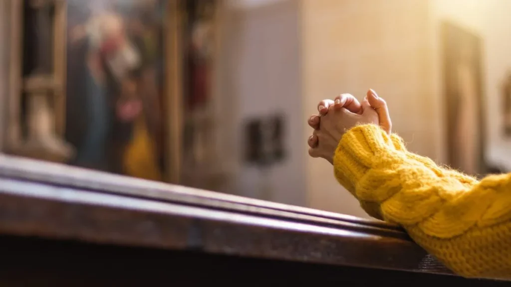 Imagem pessoa ajoelhada rezando com as maos postas na igreja do artigo É recém-convertido? Saiba 5 dicas do Papa para viver bem a fé!