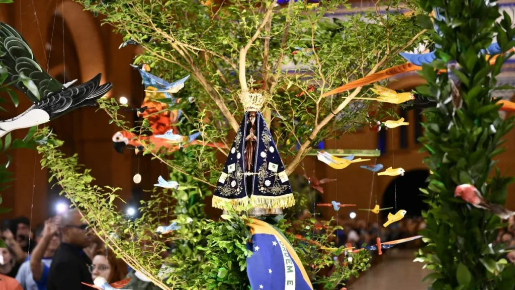 Imagem entrada do carro andor com a imagem de nossa senhora aparecida um franciscano a bandeira do brasil e flores e animais durante 2 dia da novena da padroeira 2025 do artigo Com Maria, Novena Solene reflete cuidado com a vida e a criação