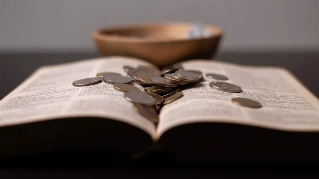 Imagem dinheiro em moedas espalhado sobre a biblia do artigo Reflexão Semanal: ninguém pode servir a dois senhores