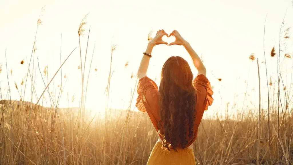 Imagem Mulher feliz fazendo coracao com as maos para a natureza do artigo De Bem com a Vida: Como aceitar nossas vulnerabilidades?
