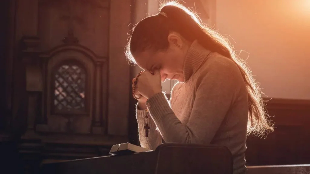 Imagem mulher rezando com o terco e a biblia dentro de uma igreja do artigo Reflexão Semanal: como viver a humildade e o amor ao próximo