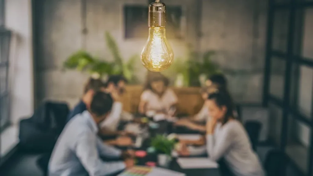 Imagem pessoas em uma mesa tendo ideias e uma lampada esta na frente deles do artigo Como trabalhar com marketing e servir com propósito?
