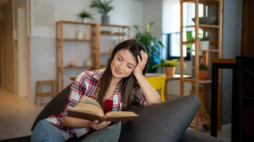 Imagem mulher lendo livro no sofa sorrindo do artigo Comece o ano com uma leitura que provoca o coração