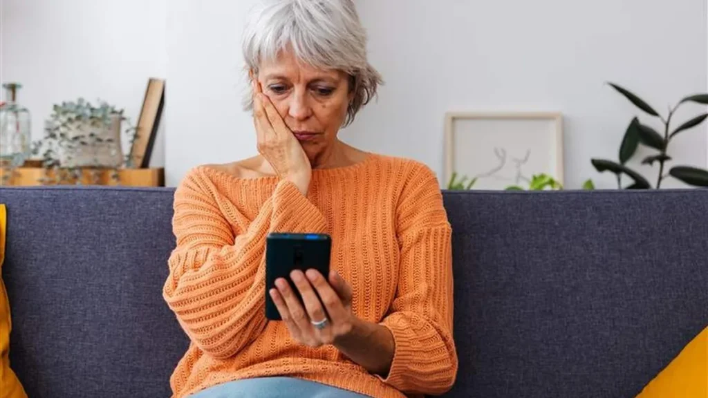 Imagem mulher sentada no sofa com celular na mao solidao do artigo Solidão silenciosa: por que é importante vencer o isolamento?
