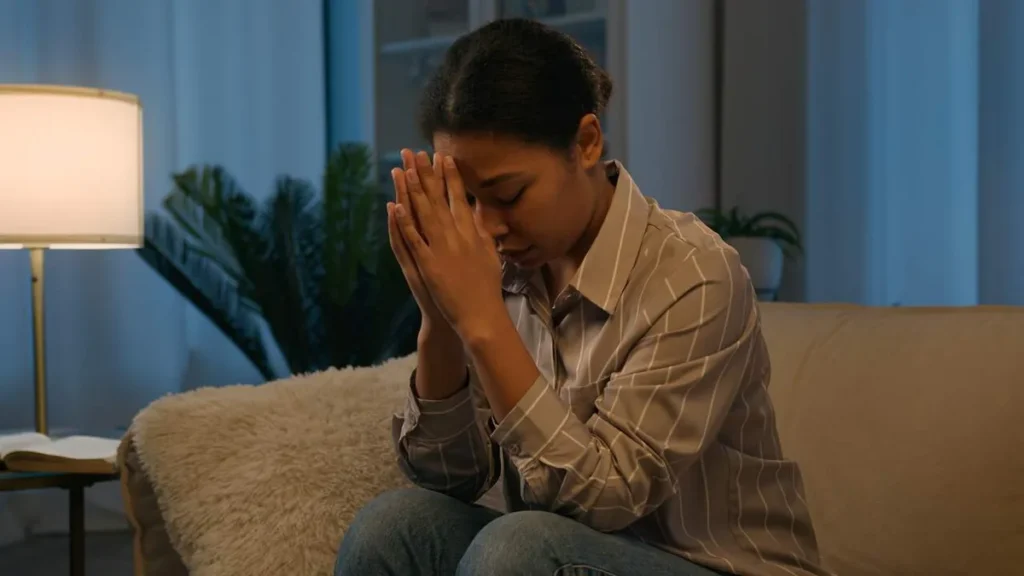Imagem mulher de cabeca baixa rezando no sofa do artigo Quando rezar parece difícil, o que fazer?