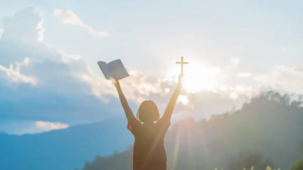 Imagem Mulher com as maos levantadas carregando um livro e uma cruz do artigo Qual a missão da Igreja após o Jubileu da Esperança?