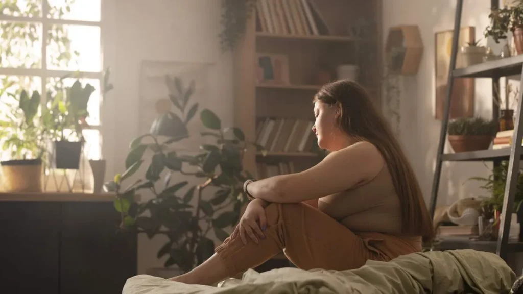 Imagem Mulher obesa sentada na cama com feicao triste do artigo Obesidade x Alzheimer: o que a ciência começa a revelar?