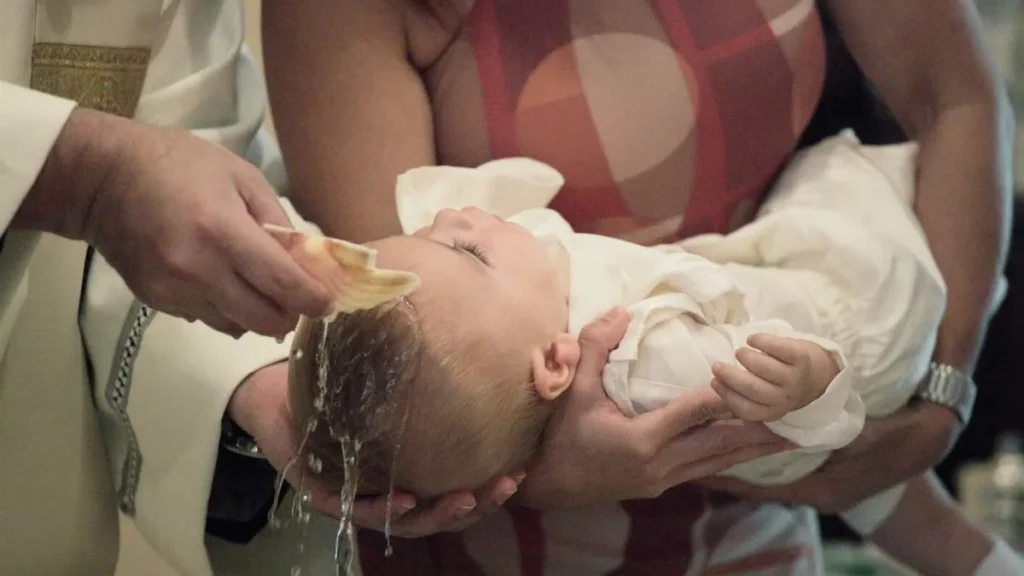 Imagem bebe menino sendo batizado segurado pela madrinha de batismo do artigo Batismo: quem pode ser padrinho ou madrinha e outras dúvidas!