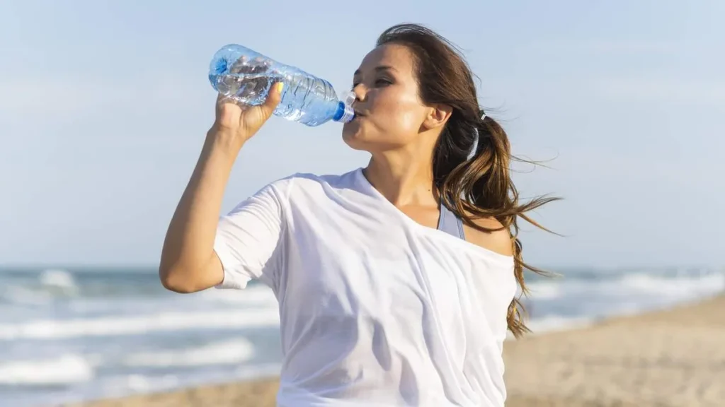 Imagem mulher bebendo agua na praia do artigo Calor em alerta: os riscos do verão para a saúde dos rins