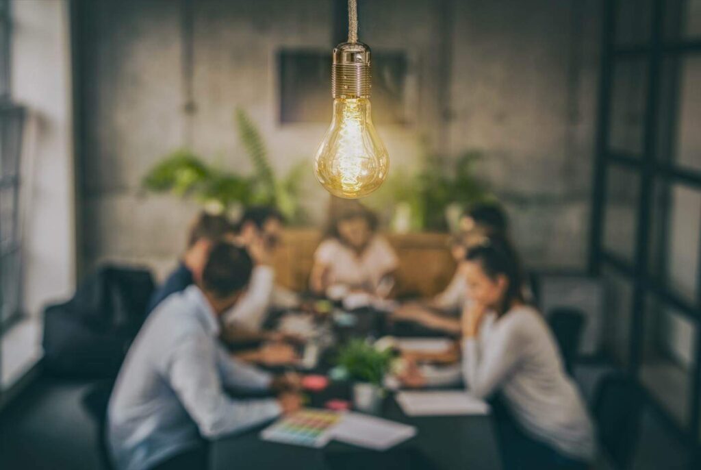 pessoas em uma mesa tendo ideias e uma lampada está na frente deles (REDPIXEL/Adobe Stock)