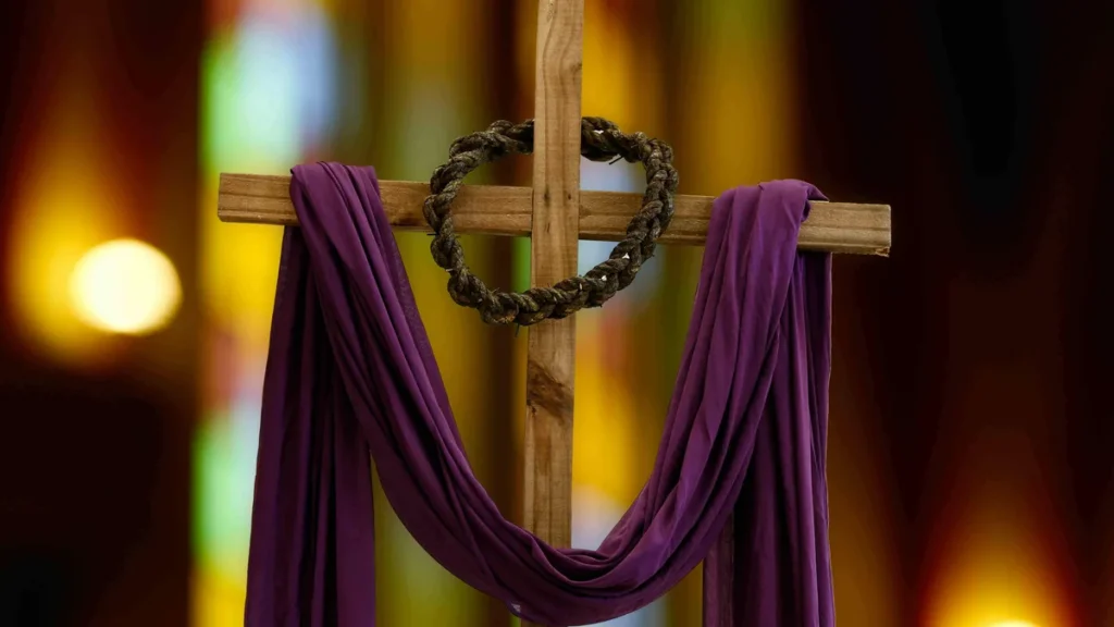 Imagem cruz de Cristo com tecido roxo e corda em volta da madeira do artigo Mistérios da Fé: entenda a Quaresma e seus símbolos