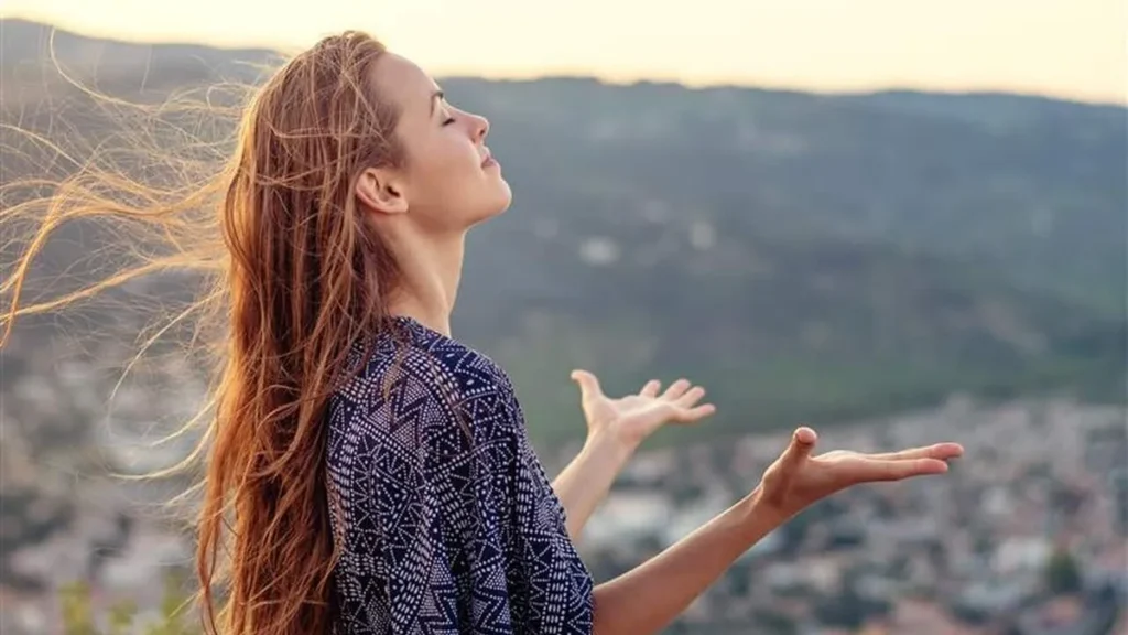 Imagem mulher com bracos abertos em oracao do artigo Falando com Deus: a relação entre a oração e a saúde do ser