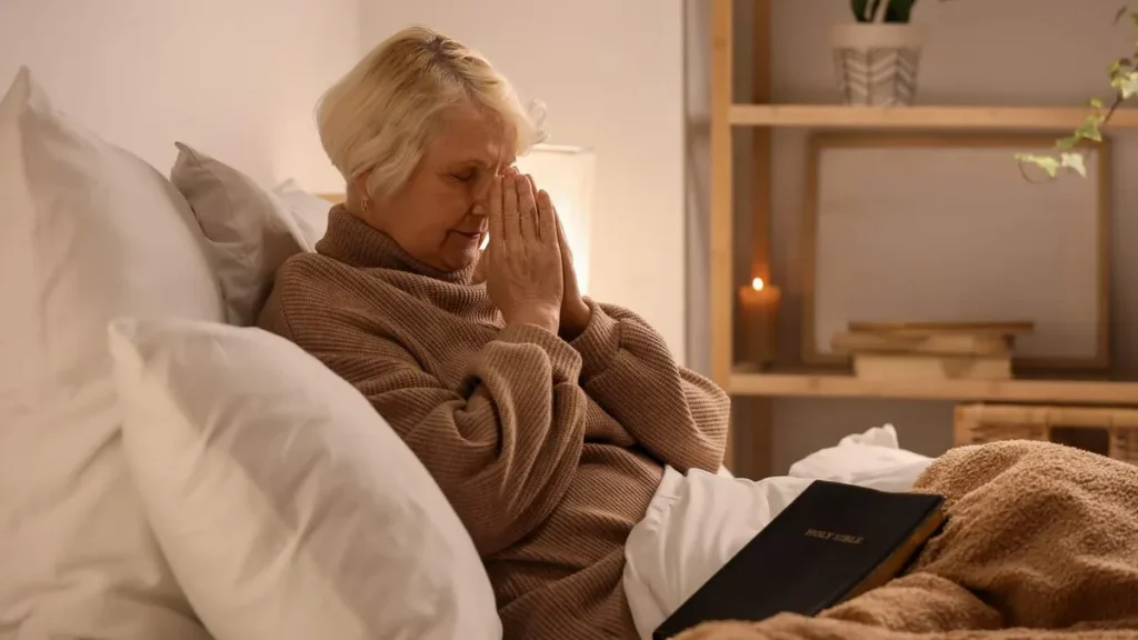 Imagem mulher rezando sentada na cama do artigo Espiritualidade: bem-estar ou encontro com Deus?