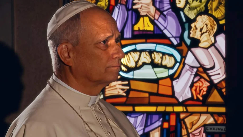 Imagem papa em video de intencao de oracao de abril sentado em frente a um vitral do artigo Papa pede oração por sacerdotes em crise