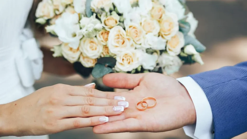 Imagem casal com maos estendidas com as aliancas na palma da mao do noivo ao fundo a noiva segura o buque do artigo A Igreja Católica realiza casamentos na Quaresma?