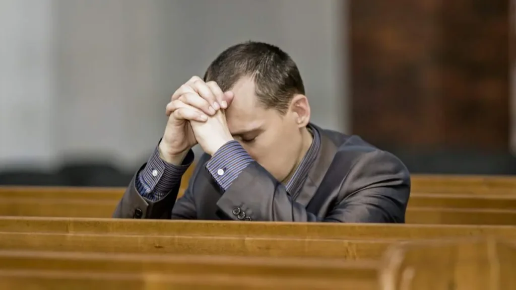 Imagem homem de roupa social ajoelhado rezando em igreja do artigo Todo pecado pode ser perdoado? Existe algum imperdoável?